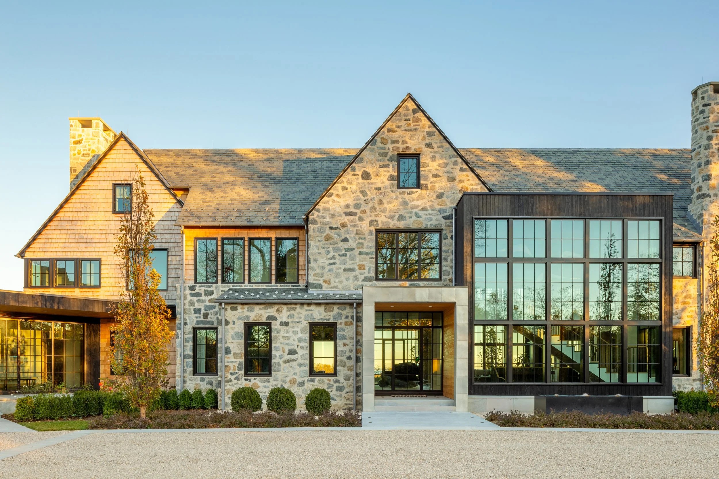 A large stone house with a spacious driveway surrounded by greenery